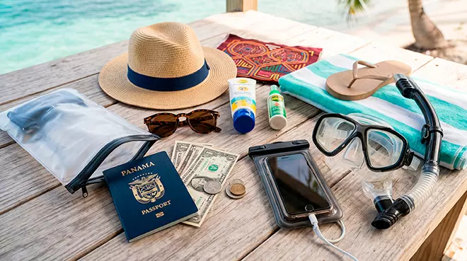 Pasaporte de Panamá, dólares en efectivo, bloqueador solar "reef-safe", sombrero de paja y equipo de snorkel organizados sobre una mesa de madera frente al mar caribeño.